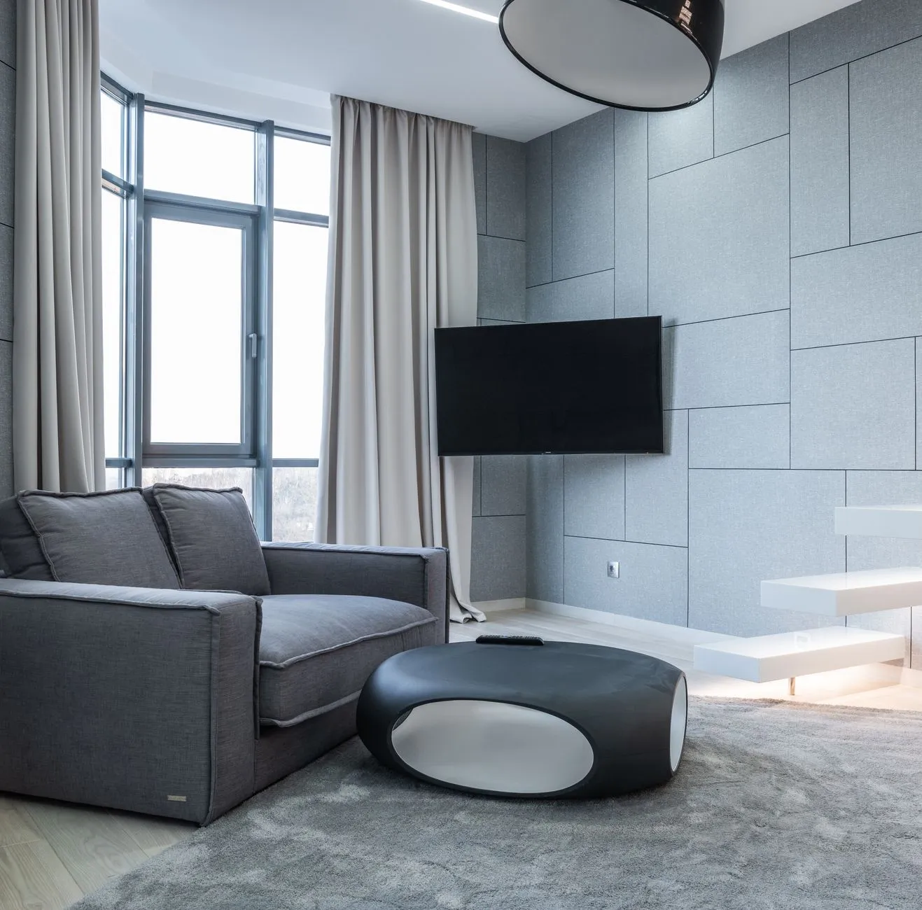 Telewizor na ścianie w nowoczesnym salonie z szarą sofą