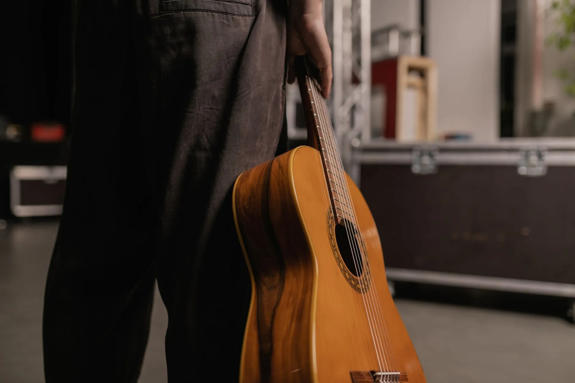 Osoba trzyma gitarę akustyczną na zapleczu sceny
