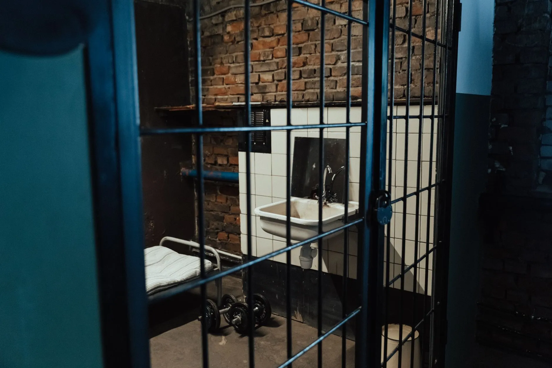 Cela więzienna z łóżkiem, umywalką i kratami